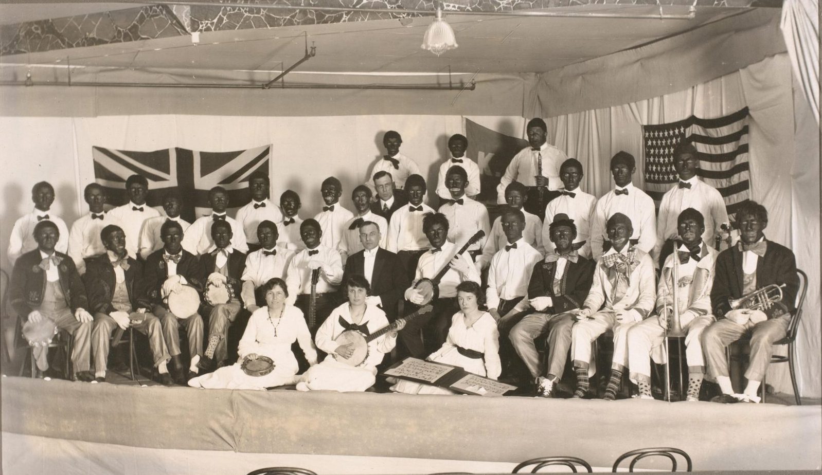 Item is a group portrait of a minstel show cast, post on stage, most of whom are white performers in blackface.
