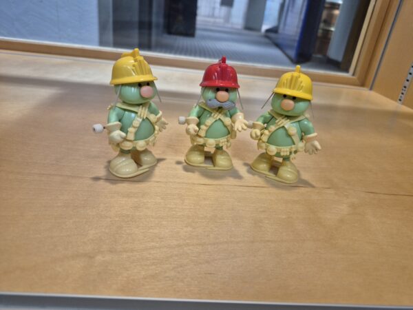 Three small green plastic figures with hard hats on.