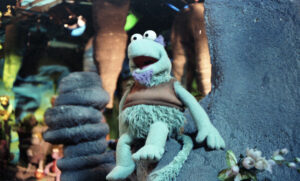 Green Fraggle puppet perched on a rock.