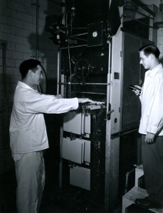 Employees operating Pako Corp. Filmachine, ca. 1950-1960. Due to strict environmental controls and low lighting, employees often wore clean white uniforms and carried “safe” flashlights, much like these two employees in the film processing department.