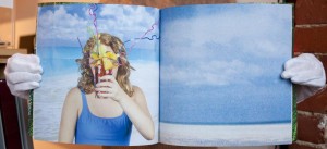 Double page spread, beach scene with blue sky and a woman in a bathing suit holding an elaborate cocktail