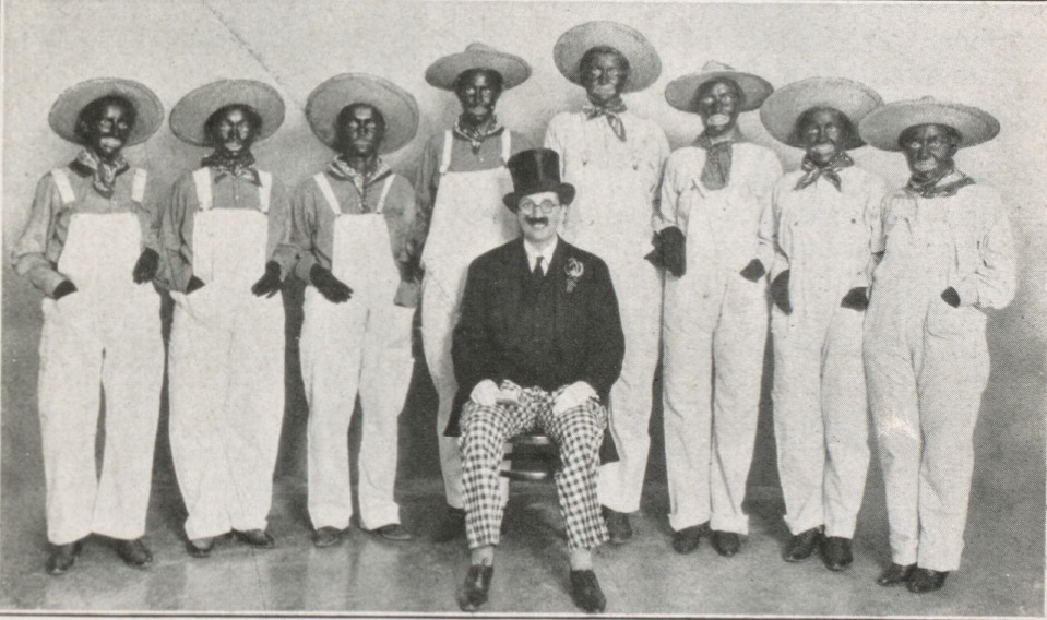 A group portrait of an all female, white minstrel show cast, 8 of whom are in blackface, one who is dressed in top hat and tails.