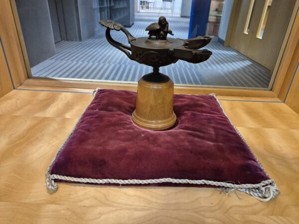 metal oil lamp on a cylindrical wood base. It is sitting on a red velvet pillow