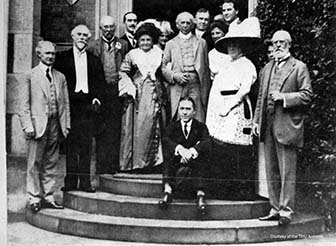 Photograph of a large group of people seated and standing in front of a building