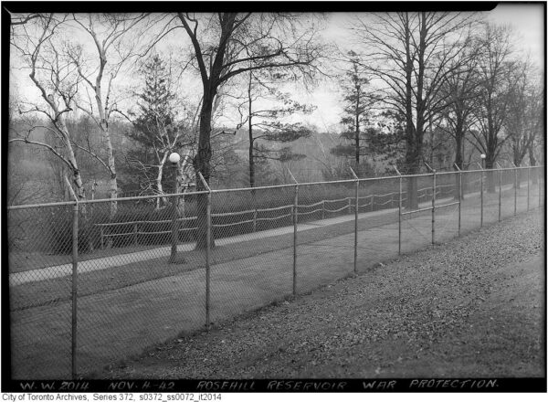 Chain link fence with barbed wire along top. Trees and a roadway on the other side.