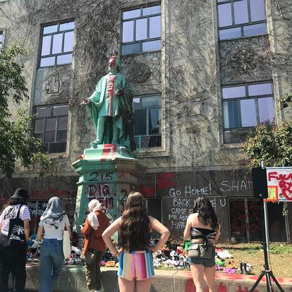 Egerton Ryerson statue with red paint splashes and several protesters standing in front.